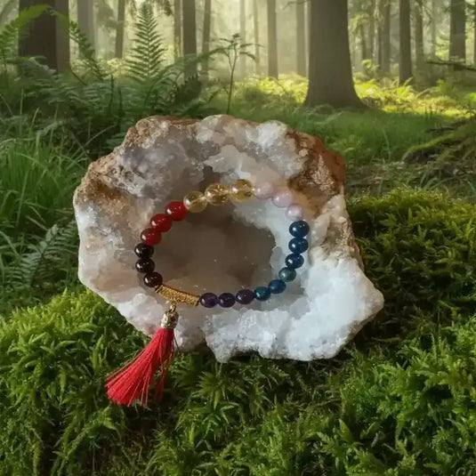 Bracelet 7 chakras dans une géode de cristal de roche reposant sur tapis de mousse fraiche et forêt en arrière plan